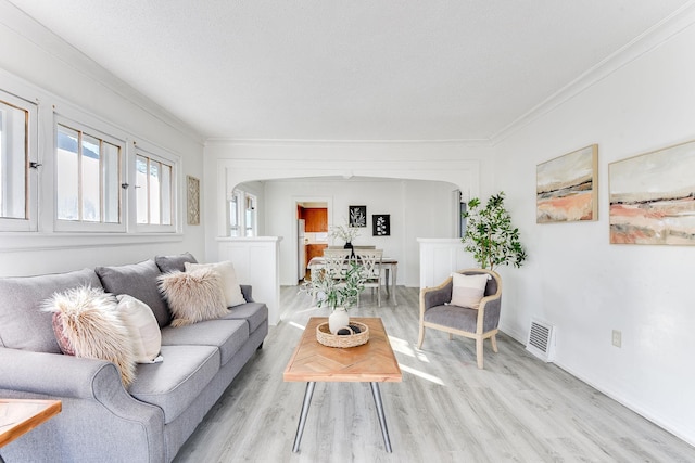 living room featuring ornamental molding, arched walkways, visible vents, and light wood finished floors