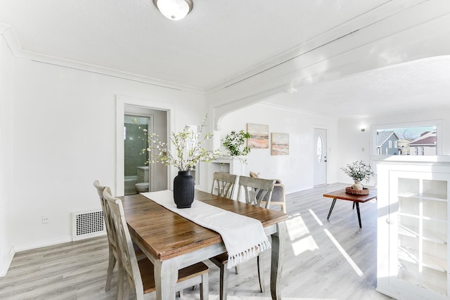 dining room featuring baseboards, visible vents, arched walkways, ornamental molding, and light wood-style floors