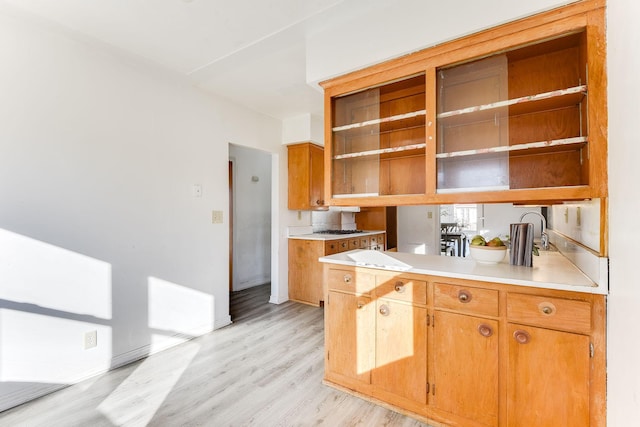 kitchen featuring a peninsula, light wood-style floors, light countertops, open shelves, and brown cabinetry