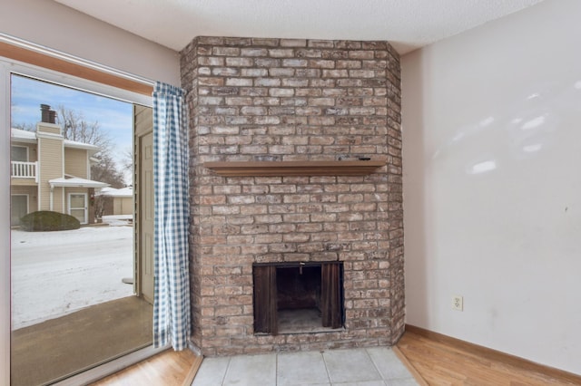 unfurnished living room featuring baseboards, a textured ceiling, a brick fireplace, and light wood-style floors