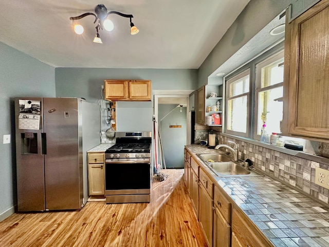 kitchen featuring a sink, appliances with stainless steel finishes, tile counters, decorative backsplash, and light wood finished floors