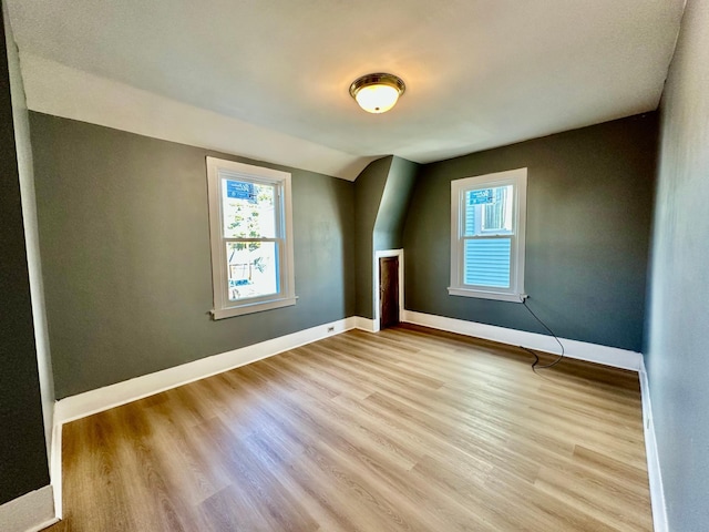 empty room with vaulted ceiling, plenty of natural light, light wood-style flooring, and baseboards
