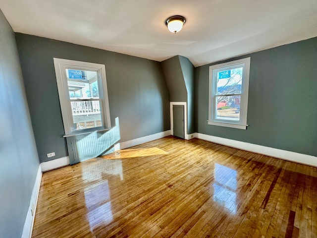empty room with light wood-style floors, vaulted ceiling, and baseboards