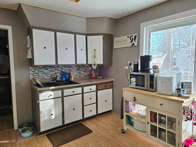 kitchen featuring decorative backsplash, stainless steel microwave, a sink, and light wood finished floors