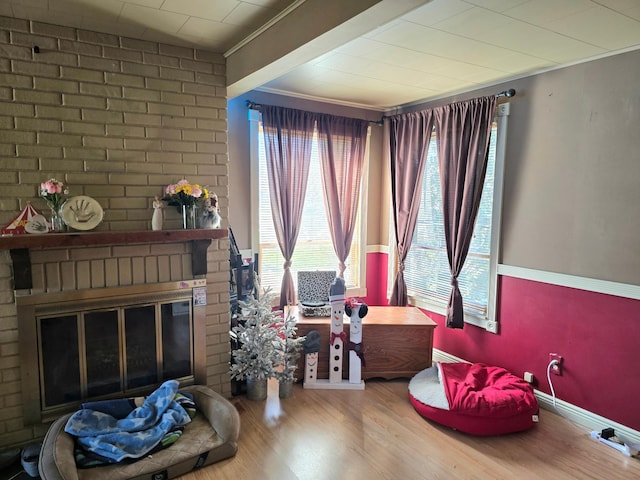 sitting room with a brick fireplace, plenty of natural light, wood finished floors, and crown molding
