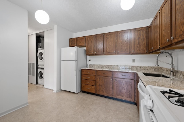 kitchen featuring a textured ceiling, white appliances, a sink, hanging light fixtures, and stacked washer and clothes dryer