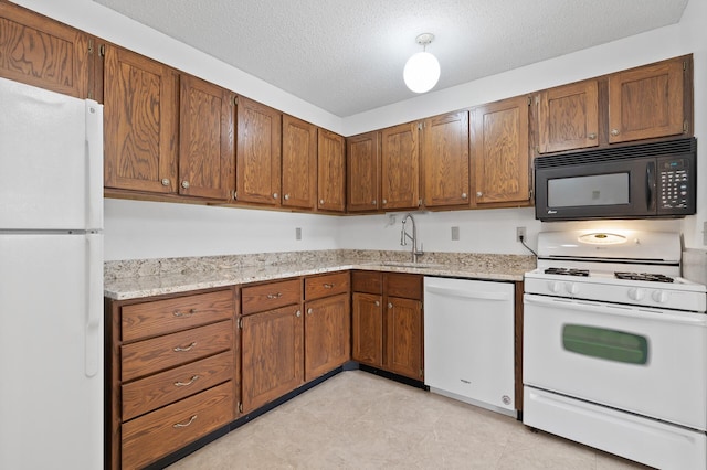 kitchen with a textured ceiling, white appliances, a sink, light stone countertops, and brown cabinetry