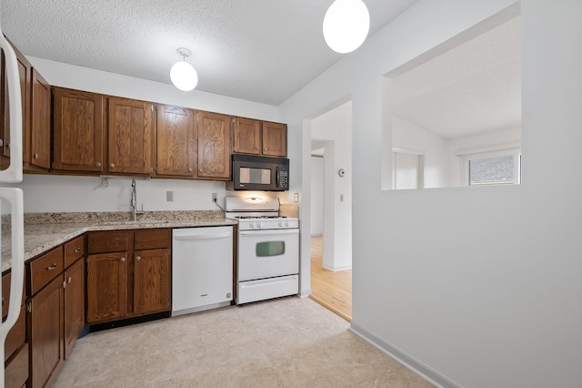 kitchen featuring white appliances, baseboards, light stone counters, a textured ceiling, and a sink