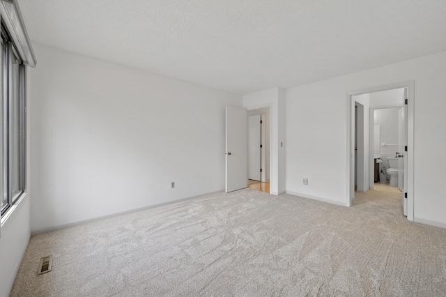 unfurnished bedroom featuring light carpet, baseboards, visible vents, and ensuite bathroom