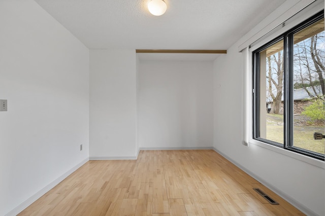 empty room with light wood-style flooring, visible vents, and baseboards