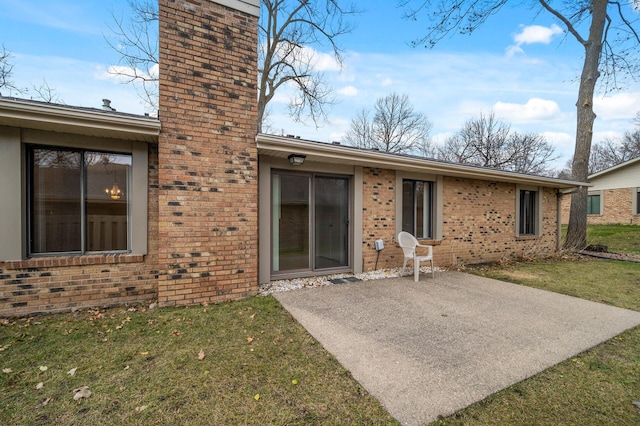 rear view of house with a patio area, a yard, a chimney, and brick siding