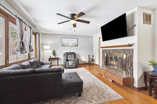 living area with visible vents, a ceiling fan, a glass covered fireplace, wood finished floors, and a textured ceiling