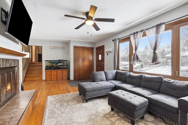 living area with a fireplace, ceiling fan, a textured ceiling, light wood-type flooring, and stairs