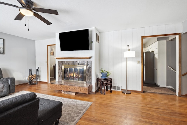 living room featuring ceiling fan, visible vents, wood finished floors, and a glass covered fireplace