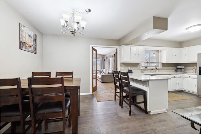 kitchen with a breakfast bar area, a peninsula, white cabinetry, light countertops, and dark wood-style floors