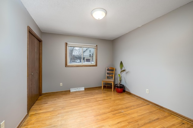 unfurnished room featuring light wood finished floors, baseboards, visible vents, and a textured ceiling