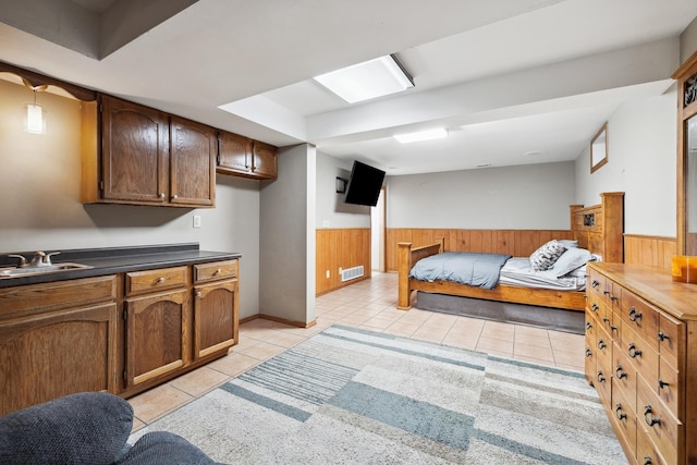 bedroom with light tile patterned floors, wooden walls, visible vents, a wainscoted wall, and a sink