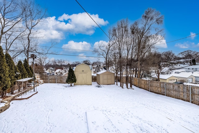 yard covered in snow with a storage shed, a fenced backyard, a residential view, and an outbuilding