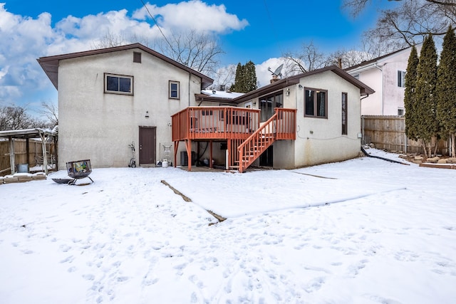 snow covered property with stairs, fence, a wooden deck, and stucco siding