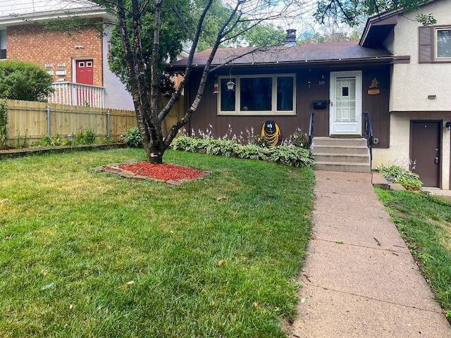 tri-level home with entry steps, fence, and a front lawn