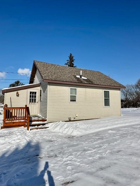 snow covered back of property featuring a shingled roof