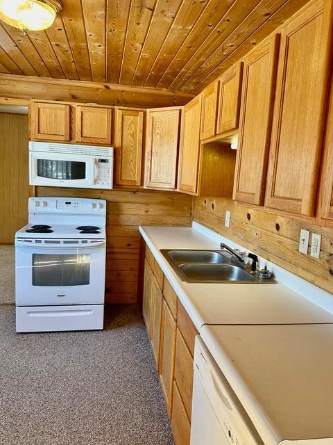 kitchen featuring light countertops, wooden ceiling, a sink, wooden walls, and white appliances