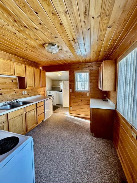 kitchen with white appliances, light colored carpet, wooden ceiling, wood walls, and a sink