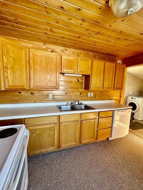 kitchen featuring light countertops, washer / clothes dryer, wooden ceiling, and a sink