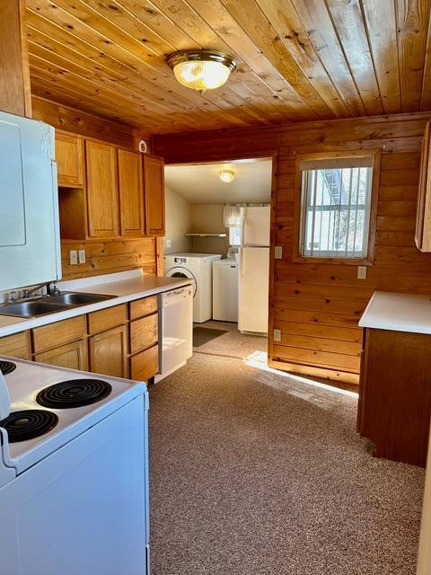 kitchen with white appliances, wood ceiling, washing machine and clothes dryer, light countertops, and a sink