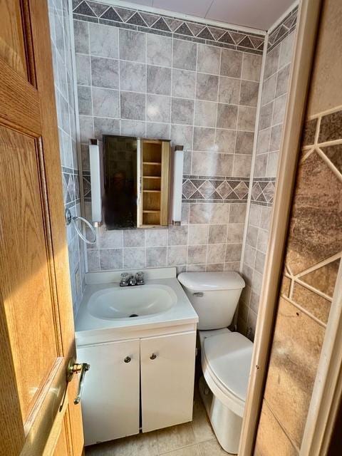 bathroom with tile patterned flooring, toilet, tile walls, and vanity