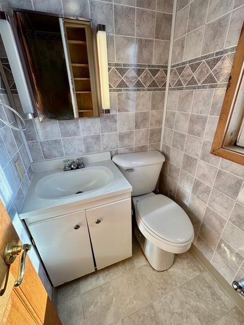 bathroom with toilet, tile patterned flooring, tile walls, and vanity