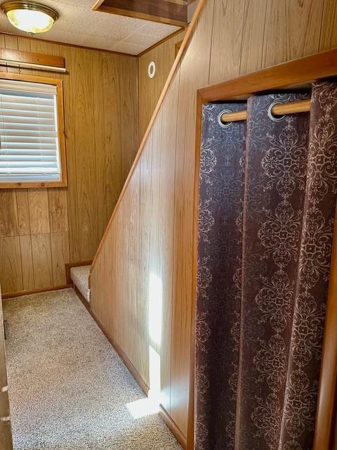 hall featuring a textured ceiling, carpet floors, stairway, and wood walls