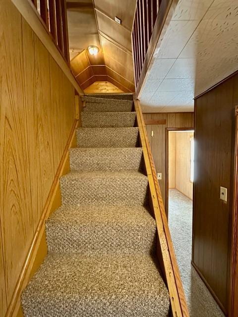 stairway featuring carpet, wood walls, and lofted ceiling