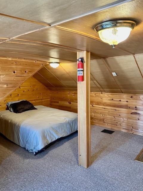 bedroom featuring vaulted ceiling, carpet flooring, and wooden walls