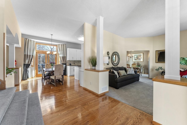 living area with a notable chandelier, visible vents, light wood-type flooring, and a textured ceiling