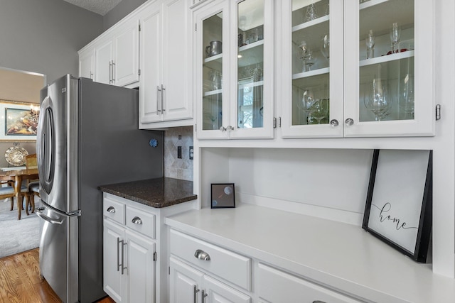 kitchen featuring white cabinets, backsplash, glass insert cabinets, and freestanding refrigerator