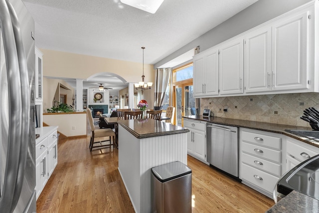 kitchen with arched walkways, white cabinets, stainless steel appliances, and light wood-type flooring