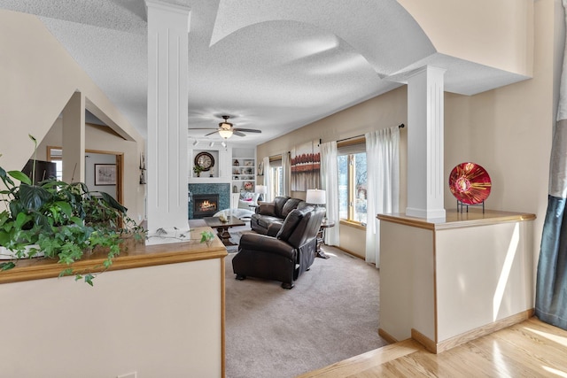 living area featuring built in features, a ceiling fan, ornate columns, a lit fireplace, and a textured ceiling