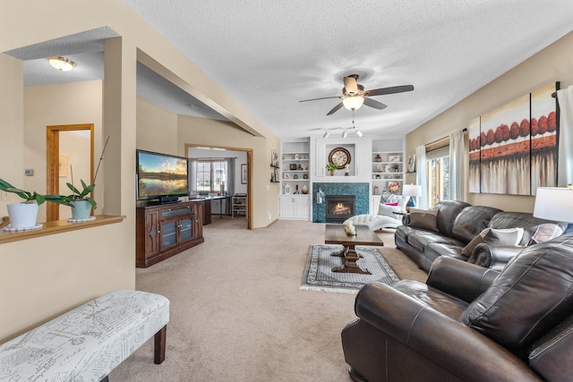 living room with built in features, light carpet, a fireplace, a textured ceiling, and a ceiling fan