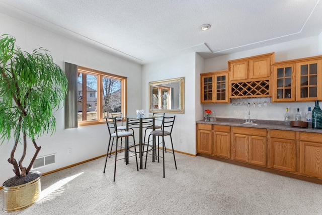 dining room with baseboards, visible vents, wet bar, a textured ceiling, and light carpet