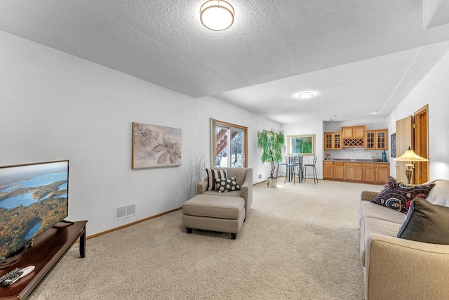 living area featuring visible vents, light carpet, a textured ceiling, and baseboards