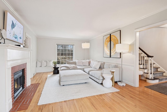 living room with baseboards, ornamental molding, wood finished floors, stairs, and a brick fireplace