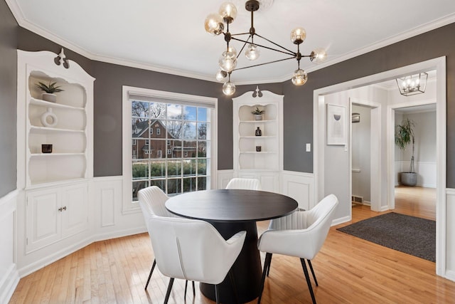 dining room featuring crown molding, a wainscoted wall, hardwood / wood-style flooring, and a notable chandelier