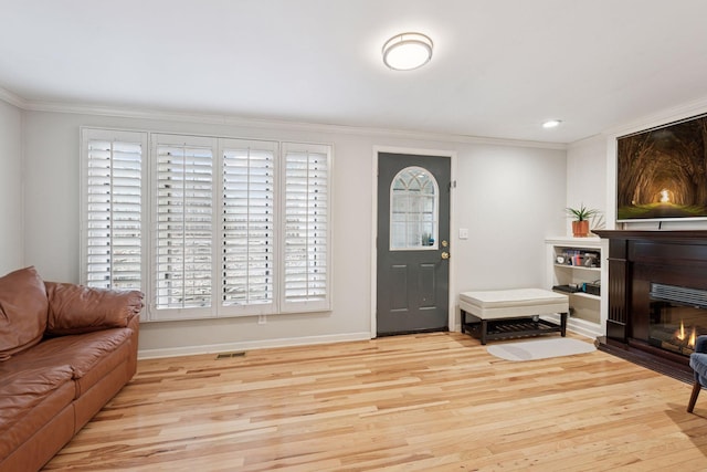 entryway with light wood finished floors, baseboards, visible vents, a glass covered fireplace, and ornamental molding