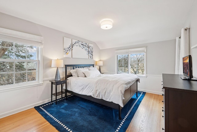 bedroom with multiple windows, vaulted ceiling, baseboards, and wood finished floors