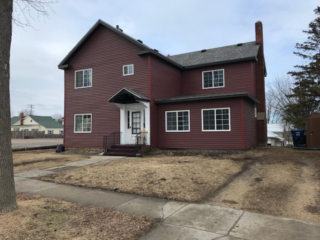 traditional home featuring roof with shingles, driveway, and a chimney