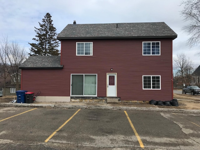 rear view of property featuring uncovered parking, entry steps, and roof with shingles