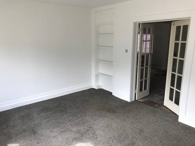 empty room with built in features, dark carpet, and baseboards