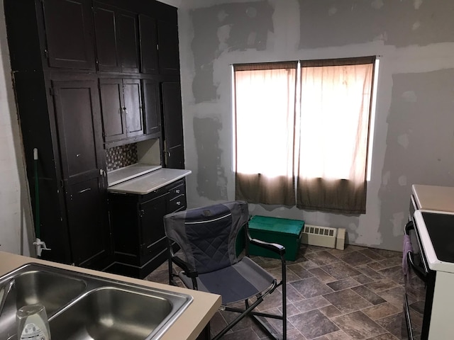 kitchen with electric range, stone finish floor, dark cabinets, light countertops, and a sink