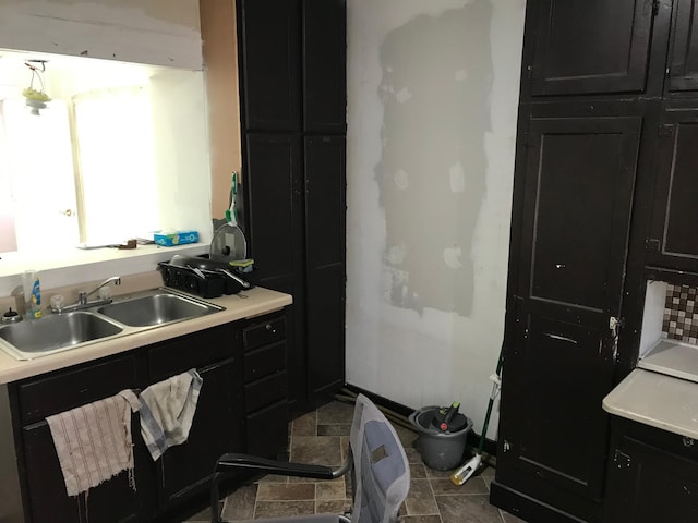 kitchen with light countertops, dark cabinetry, a sink, and baseboards